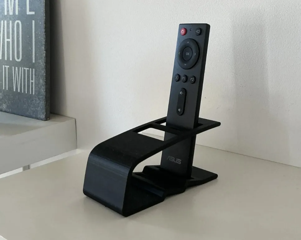 Soporte negro para control remoto sobre un estante, con un control puesto